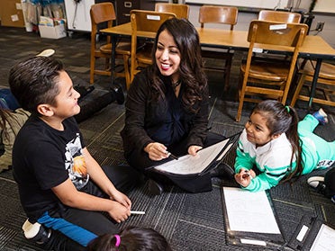 A student teacher from Georgia Southern's Department of Curriculum, Foundations and Reading and a group of students sitting on a rug discuss a worksheet.